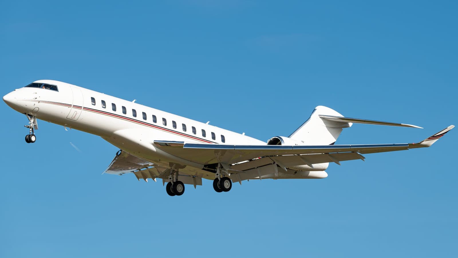 A NetJets Bombardier Global 7500, N182QS, in landing configuration against a clear blue sky, gear and flaps extended.