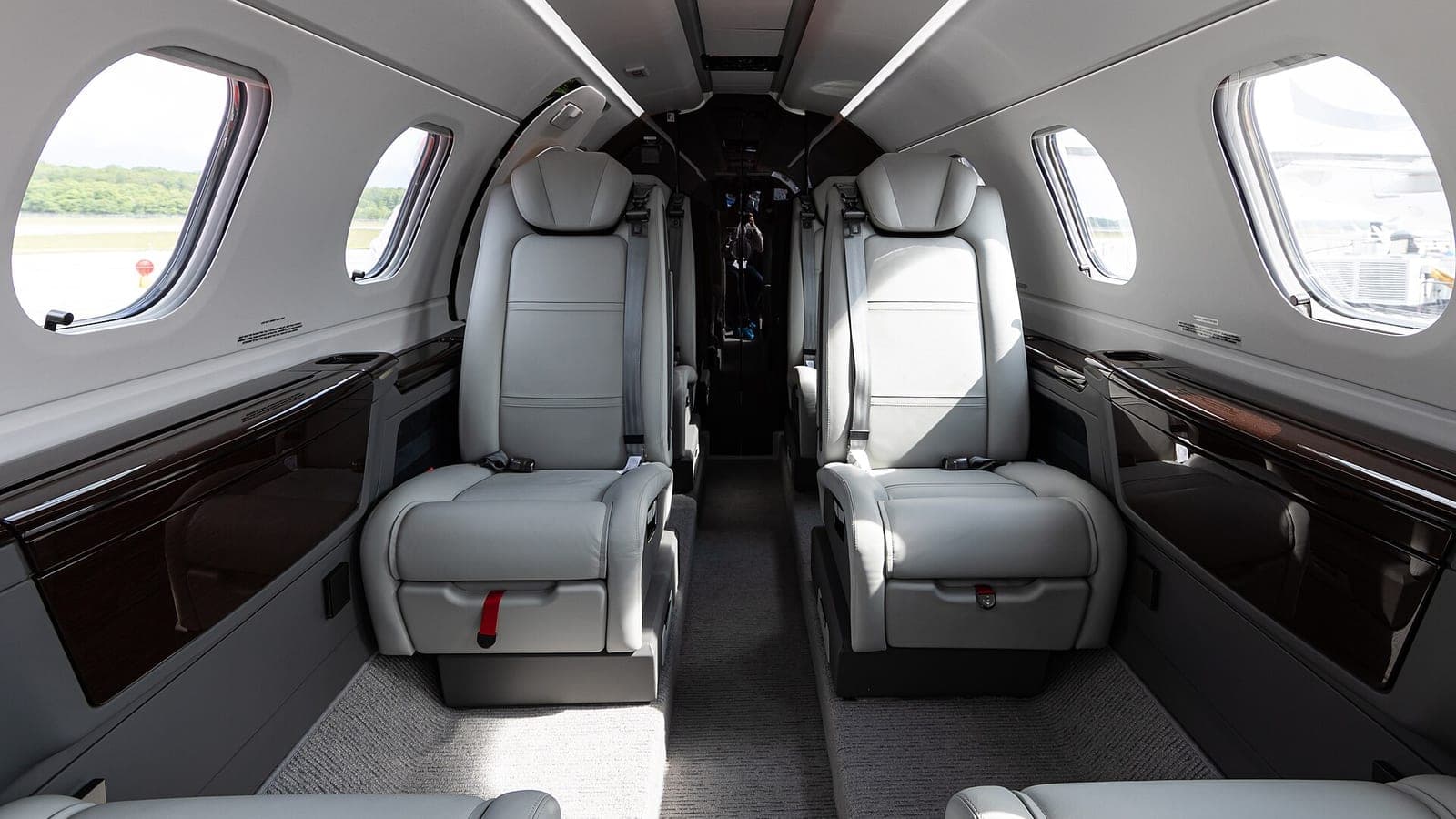 The empty cabin of an Embraer Phenom 300, looking aft down the aisle between four unoccupied pale leather seats.