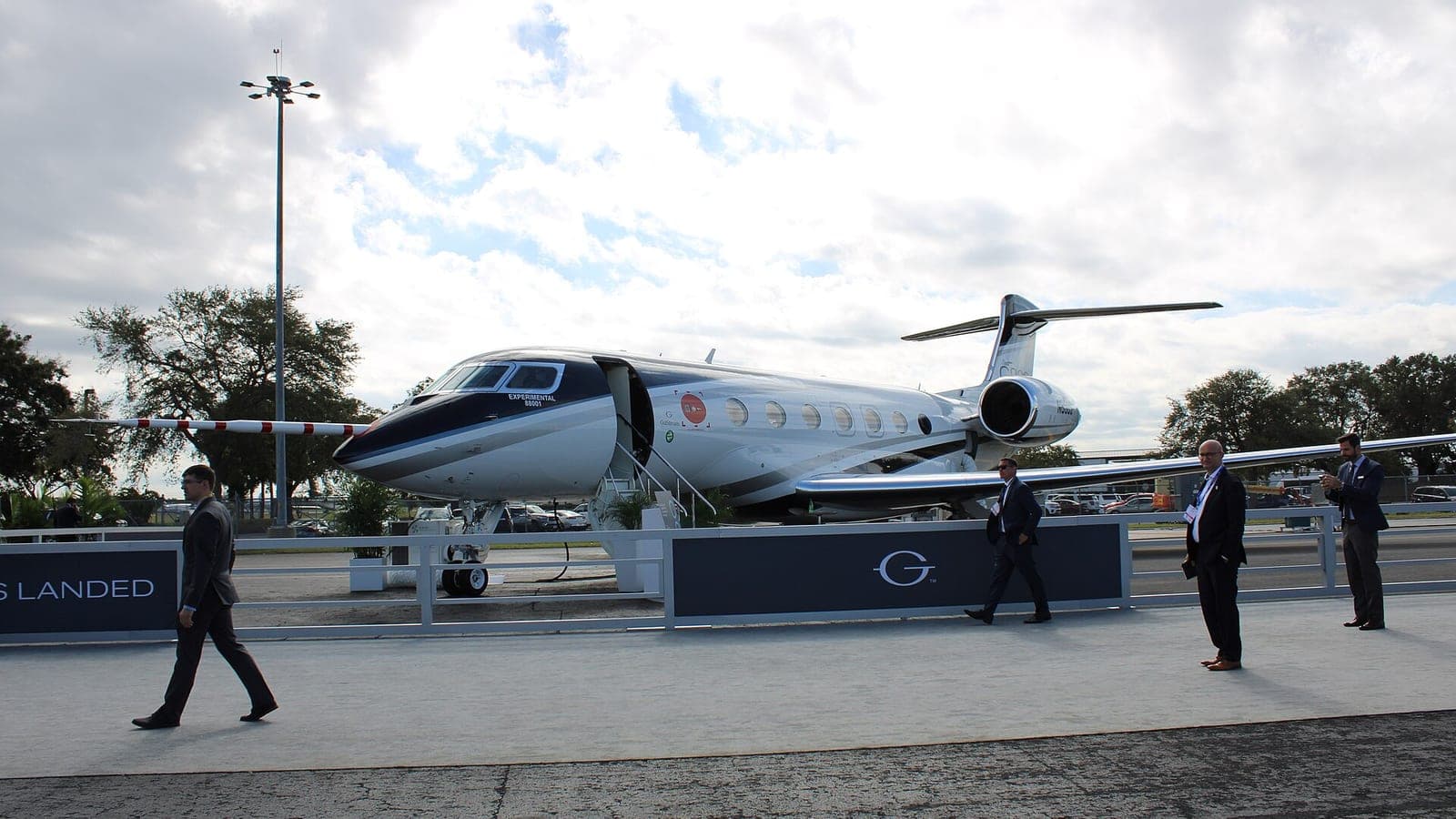 A Gulfstream G800 on static display at NBAA-BACE 2022 in Orlando, side-on with its airstair down and EXPERIMENTAL 68001 painted on the nose, behind a low show barrier that visitors in suits are walking past.