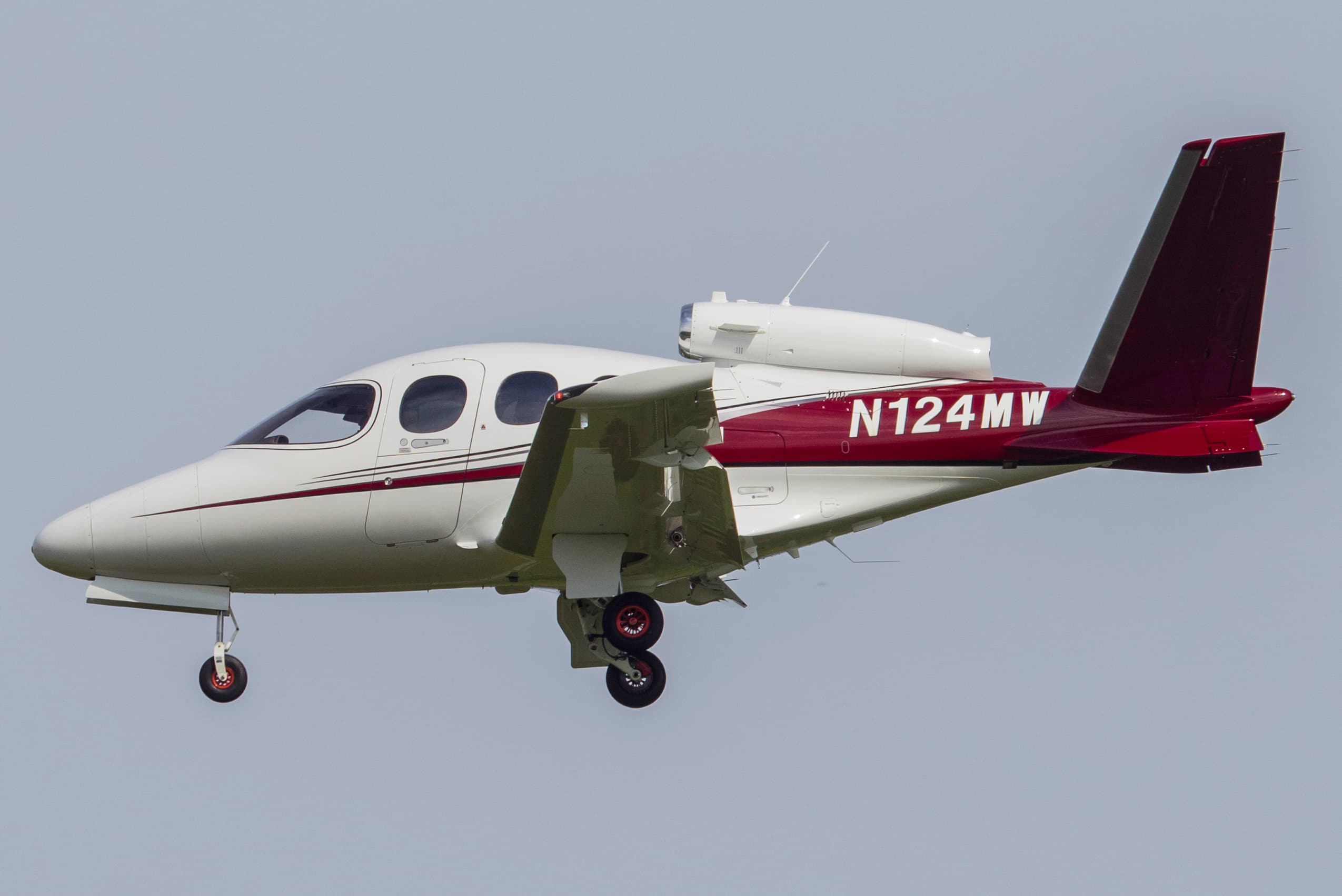 A Cirrus Vision SF50 single-engine very light jet, registration N124MW, photographed in daylight showing its V-tail and dorsal-mounted engine above the rear fuselage.