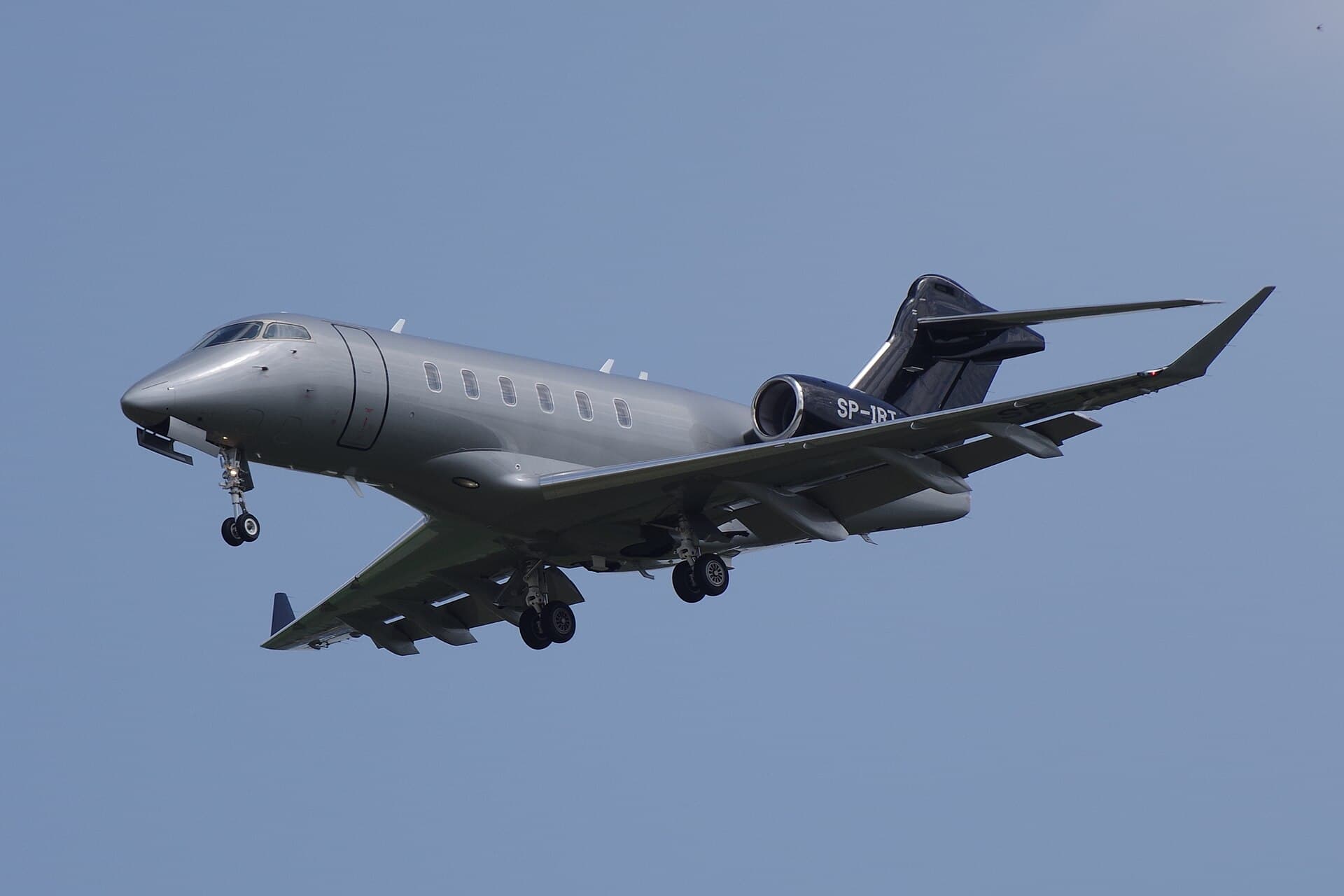 A Bombardier Challenger 3500 super-midsize business jet, registration SP-IRT, on final approach with gear down, landing at Berlin Schönefeld in daylight.