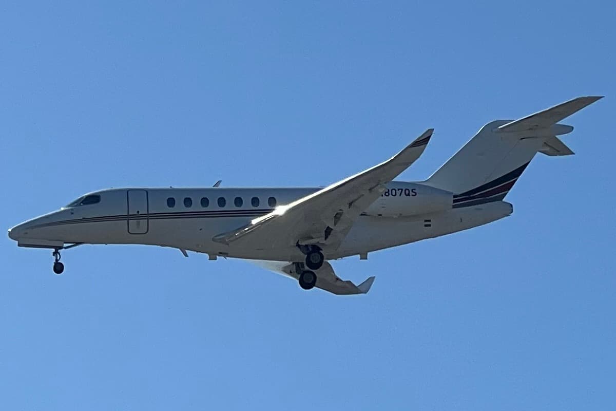 A Cessna Citation Longitude in NetJets white-and-blue livery, registration N807QS, on final approach with gear down at John Wayne Airport, Santa Ana, California, in clear daylight.