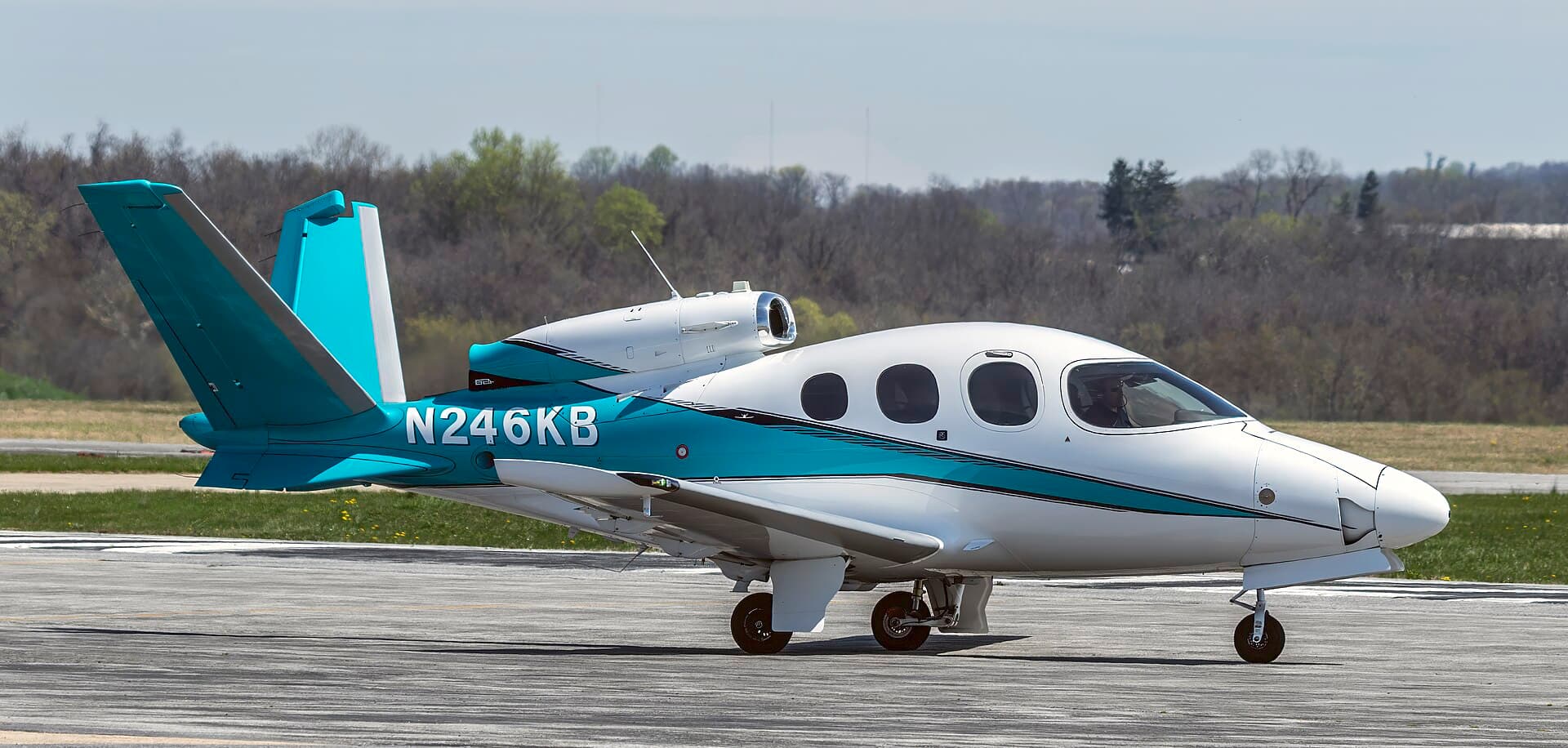 A single-engine Cirrus Vision SF50 personal jet, registration N246KB, in a mostly white scheme with its distinctive V-tail and dorsal-mounted engine, photographed in bright daylight on the ground at Frederick Municipal Airport in Maryland.