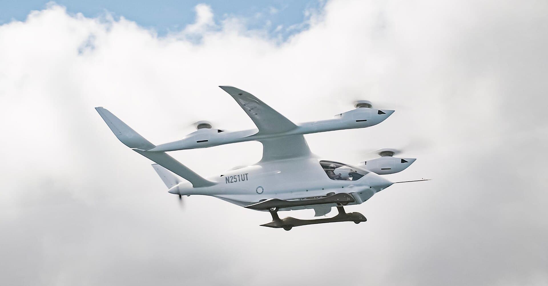 BETA Technologies' A250 eVTOL prototype, registration N251UT, airborne in daylight with its lift rotors on the wing-mounted booms and a pusher propeller at the tail.