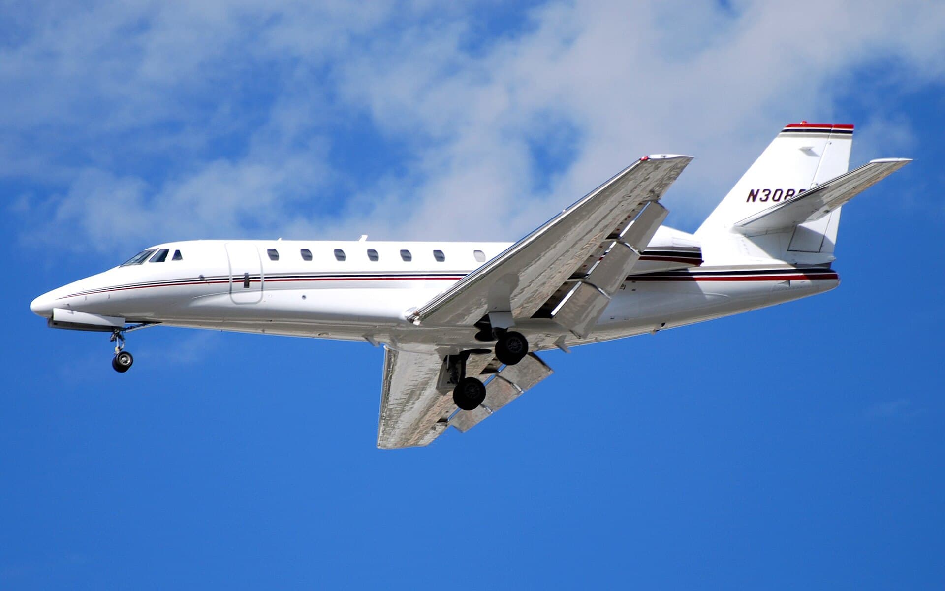 A NetJets Cessna Citation Sovereign, registration N308QS, in the fleet's white fuselage with dark blue cheatline and tail, photographed in flight on approach under bright afternoon light at Las Vegas McCarran International Airport, landing gear extended.