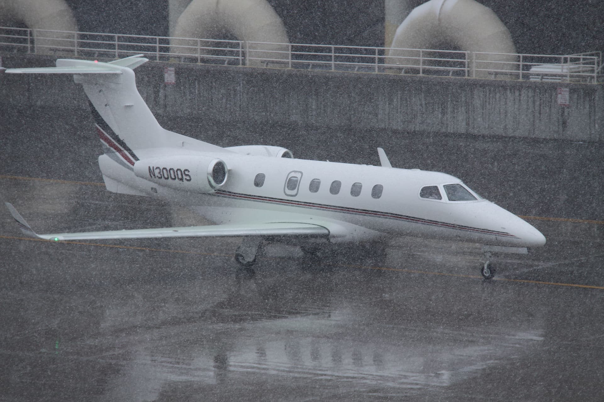 An Embraer EMB-505 Phenom 300 light business jet in NetJets' white and dark blue livery, registration N300QS, seen at Denver International Airport in daylight.