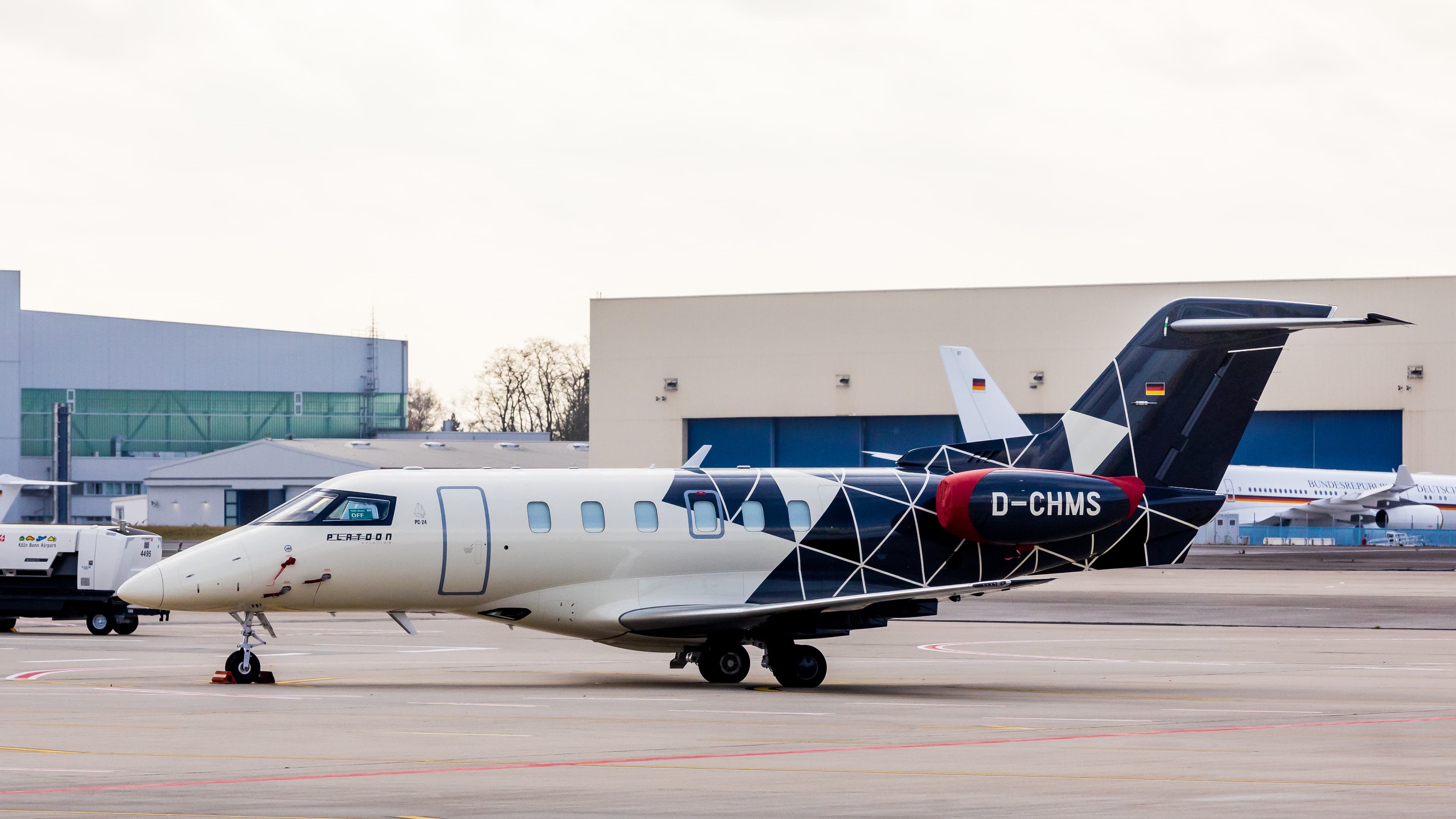 A Pilatus PC-24 twin-engine business jet, registration D-CHMS in Platoon Aviation colours, standing parked on the apron at Cologne Bonn Airport.