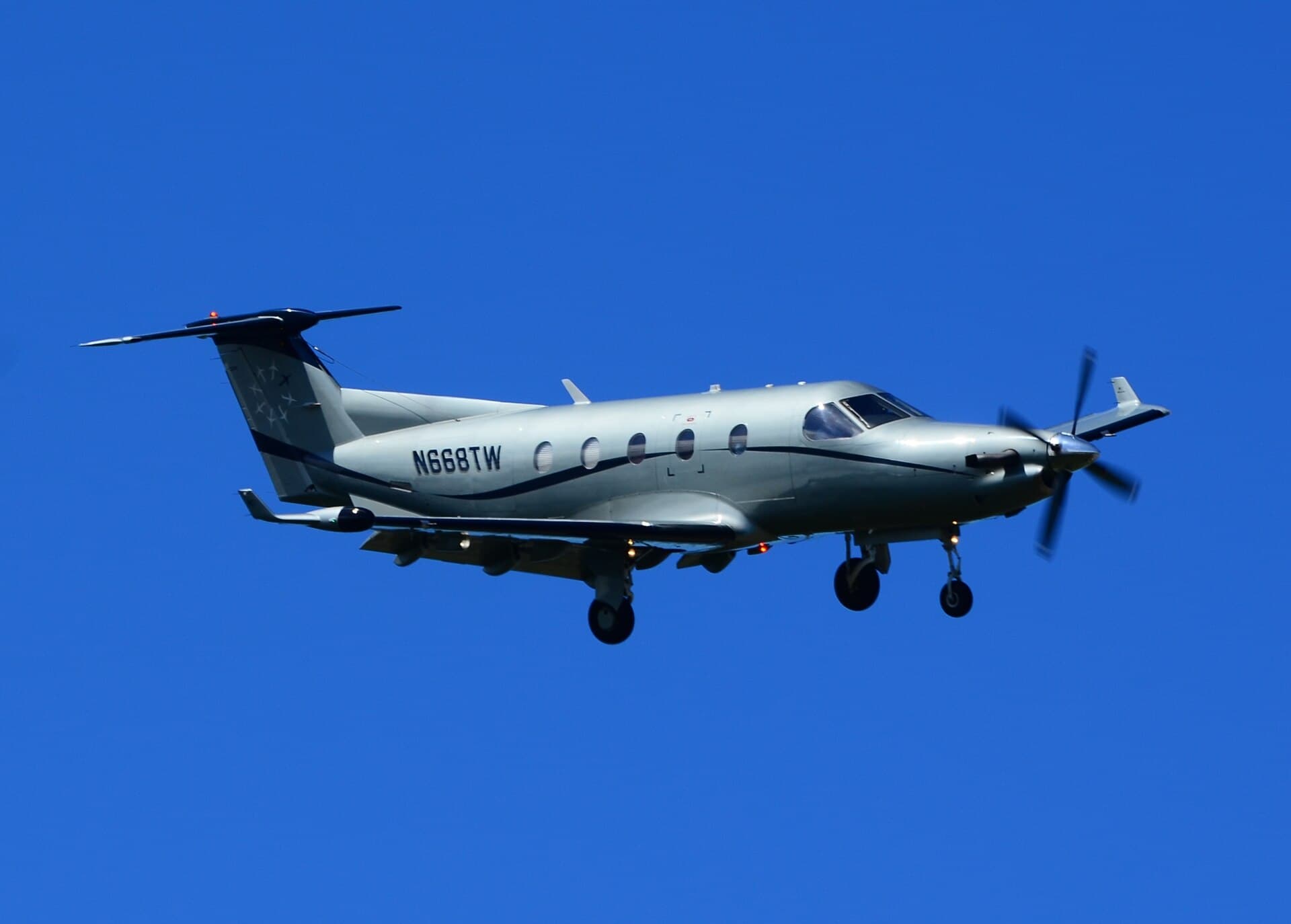 A single-engine Pilatus PC-12 turboprop registered N668TW in Tradewind Aviation's white and dark-blue livery, airborne with gear down over San Juan, Puerto Rico in bright daylight.