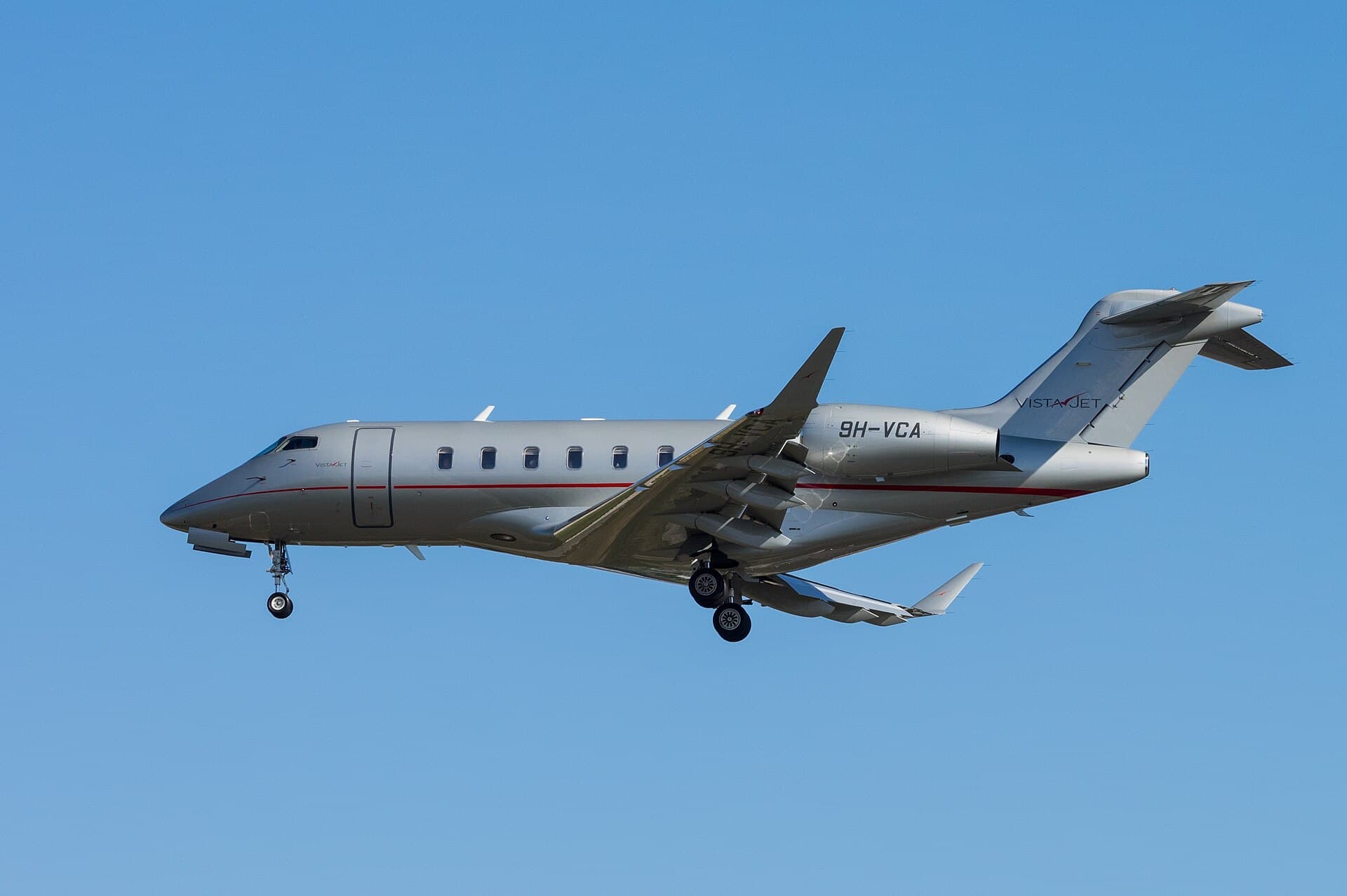 A VistaJet Bombardier Challenger 350, registration 9H-VCA, in the operator's silver-grey livery with red tail stripe, photographed on the ground at Geneva International Airport in daylight.